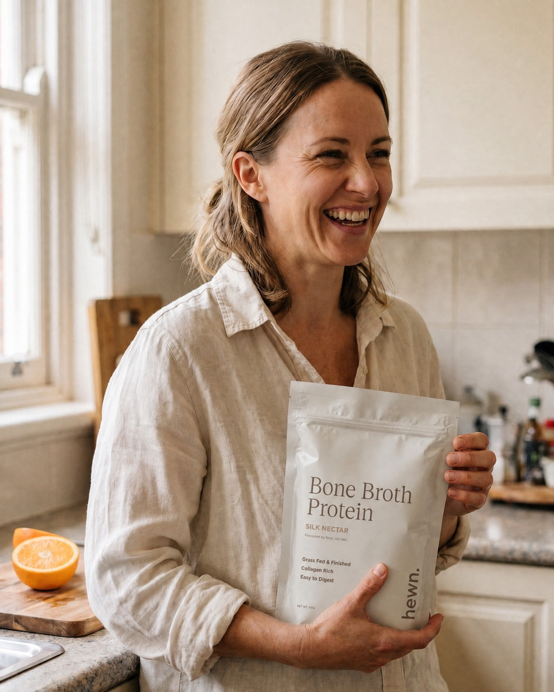 A hewn customer laughing in her kitchen, holding a bag of Bone Broth Protein