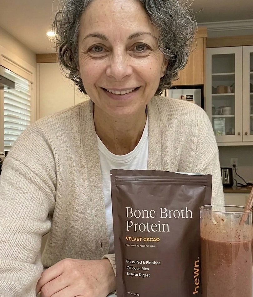 Woman in her 50s holding hewn Bone Broth Protein and a chocolate smoothie in her kitchen
